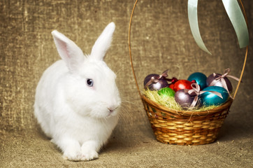 White clean beautiful Easter bunny next to a wicker basket with eggs in the background krashenyymi natural burlap cloth