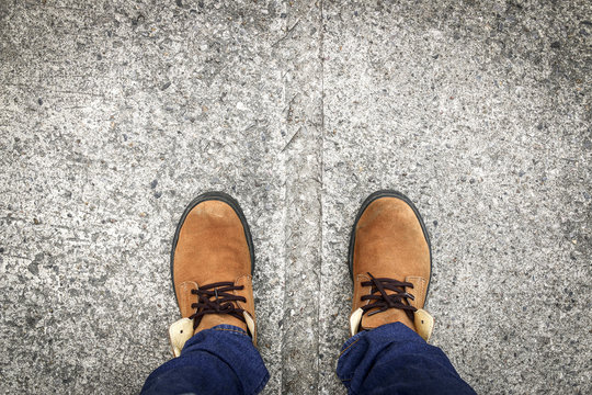 A man wears jeans and leather shoes on concrete floor background.