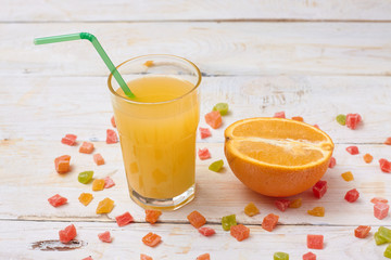 A whole orange with a glass of orange juice on white wooden background with candy in a plate.  Concept.