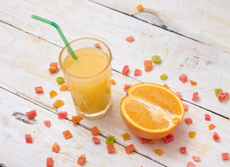 A whole orange with a glass of orange juice on white wooden background with candy in a plate.  Concept.