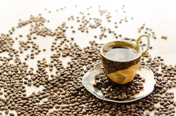 Cup of coffee surrounded by a scattered coffee beans on a wooden table - horizontal view