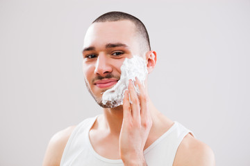 Young man is applying shaving cream to his face.