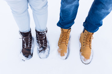 Legs and feet of couple in love in stylish shoes standing in snow