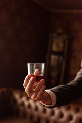 Groom holds in his hand a glass of whiskey indoors