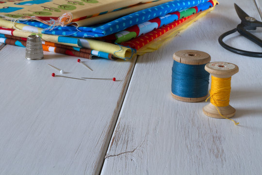 Colorful fabrics with vintage scissors, pins, measuring tape and rolling cotton threads on white wooden table