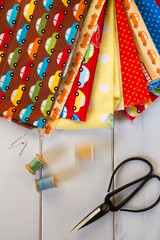 Colorful fabrics with vintage scissors, pins, measuring tape and rolling cotton threads on white...