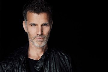Portrait of man wearing black leather jacket in front of black background