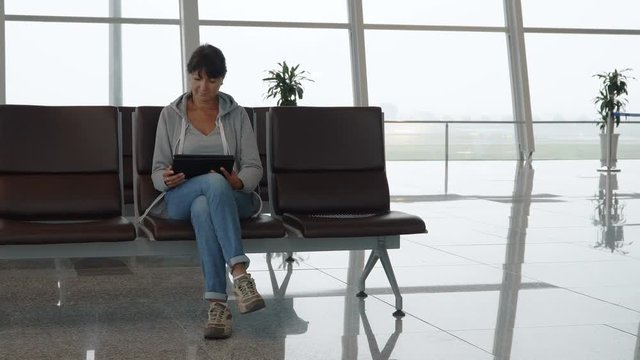 Woman using a digital tablet in empty airport waiting area. 4K people stock footage.

