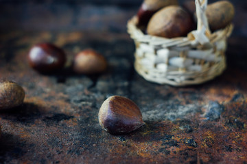 Fresh chestnuts in basket over black rustic surface.