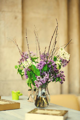 Branch with fresh blooming spring lilac flowers in vase, on table in the cafe