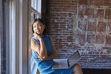 Businesswoman In Office Sitting By Window Using Laptop