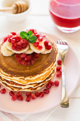 Traditional breakfast: stack of pancakes with banana slices and garnet seeds on white wooden table. Selective focus