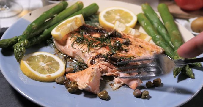 Cutting with a fork a delicious roasted organic salmon with capers and dill