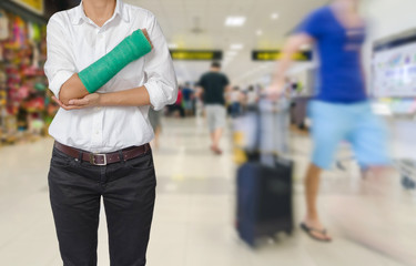 Injured woman with green cast on hand and arm on traveler in motion blur in airport interior background, ,body injury concept.