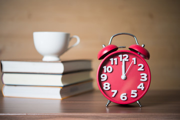 Concept of Education - Coffee cup on Pile of books with red alarm clock against wooden background.