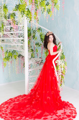 Beautiful woman in red long dress with a gold crown and earrings near forged spiral staircase