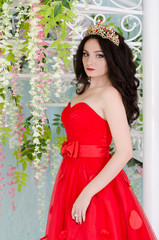 Beautiful woman in red long dress with a gold crown and earrings near forged spiral staircase