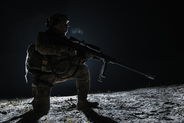 Army sniper with big rifle sitting holding rifle on black background. Lone killer in the moonlight
