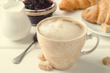 Traditional breakfast with fresh croissants and coffee on white wooden background.