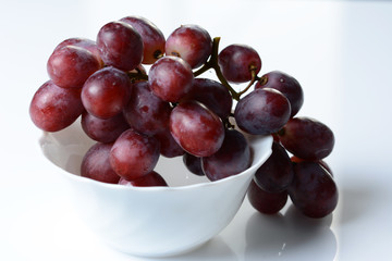 A bunch of rose grapes in a white bowl - white background