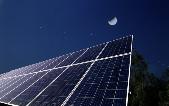 Solar panels at night with the half moon before the sun rising