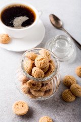 Obraz na płótnie Canvas Amaretti cookies in glass pot with white cup of coffee on light gray background with copy space. High angle view