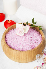 Obraz na płótnie Canvas Bath salt with aroma of a rose in a wooden bowl, petals and a fresh pink rose, towels and candles on a white background.