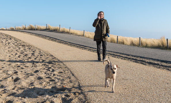 A woman walking along a coastal footpath with her dog on a clear and sunny spring day