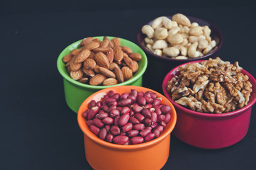 Mix of nuts in ceramic bowls on a black background. Almond, peanut, cashew and walnut.