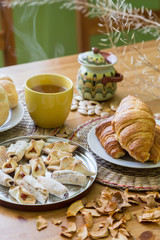 Black tea in yellow mug with croissants, buns and homemade cookies on wooden table