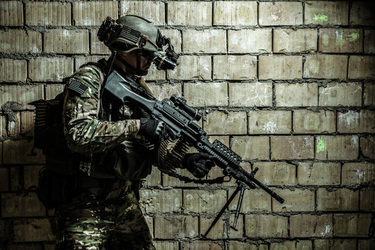 US Army Ranger member with machinegun and night vision goggles moving along the wall during mission