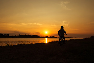 Fototapeta na wymiar Cute little boy play and riding bicycle sunset background