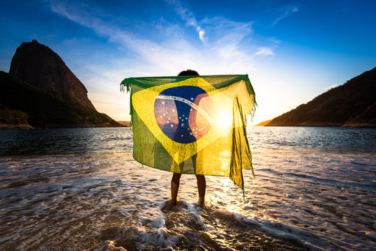 Girl Standing in Water and Holding Beach Yoke With Brazilian Flag by Sunrise, in Rio de Janeiro, With the Sugarloaf Mountain in the Horizon