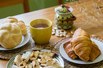 Black tea in yellow mug with croissants, buns and homemade cookies on wooden table