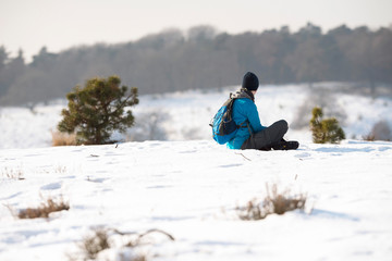Fototapeta na wymiar Man with backpack and woolen cap sitting in snow.