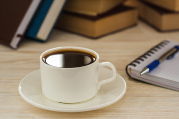 Notebook with pen on a wooden table in front of the window. A cup of hot coffee on the table.
