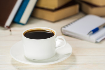 Notebook with pen on a wooden table in front of the window. A cup of hot coffee on the table.