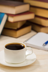 Notebook with pen on a wooden table in front of the window. A cup of hot coffee on the table.