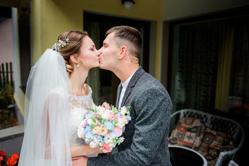 Soft kiss of stylish wedding couple standing on the porch