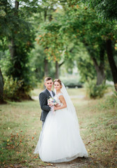 Groom in grey suit and bride pose on path in green park