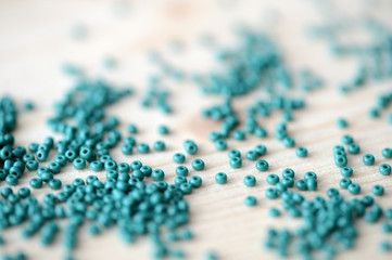Scattered seed beads of emerald color on the wooden background