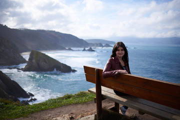 Mujer joven sentada en un banco al borde de un acantilado
