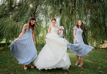 Fototapeta premium Bride and bridesmaids in blue dresses whirl on geen lawn