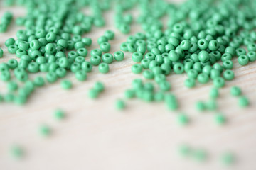 Scattered seed beads of green color on the wooden background