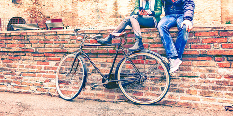 Young people with retro bike sitting on old urban wall texting message on phone - Couple of best...
