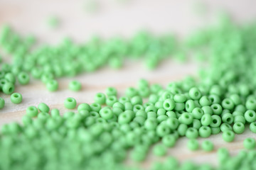 Scattered seed beads of light green color on a wooden background