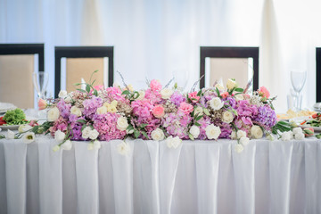 Garland of pink hydrangeas and white roses lies on long dinner table