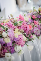 Garland of pink hydrangeas and white roses lies on long dinner table
