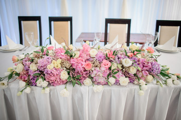Garland made of pink roses and hydrangeas lies on white dinner table