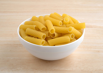 Bowl filled with rigatoni pasta on wood table.